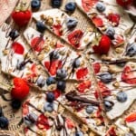Overhead view of frozen yogurt bark broken into pieces topped with berries, granola, and chocolate
