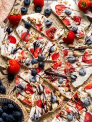 Overhead view of frozen yogurt bark broken into pieces topped with berries, granola, and chocolate