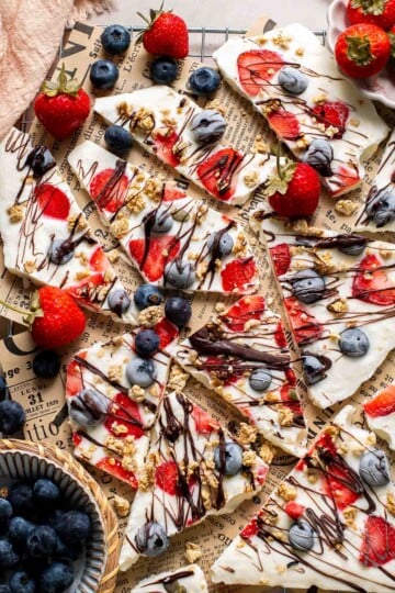 Overhead view of frozen yogurt bark broken into pieces topped with berries, granola, and chocolate