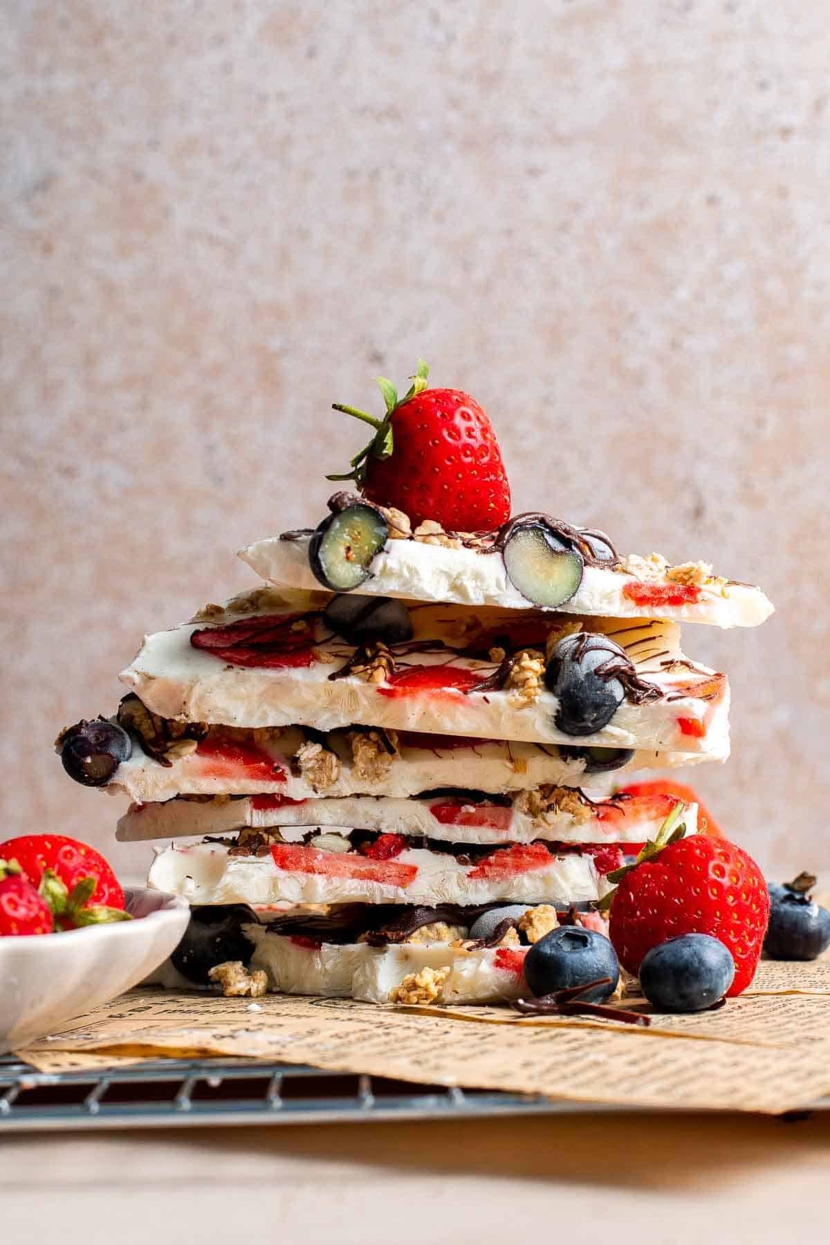 Stack of frozen yogurt bark pieces showing layers of berries, granola, and chocolate drizzle