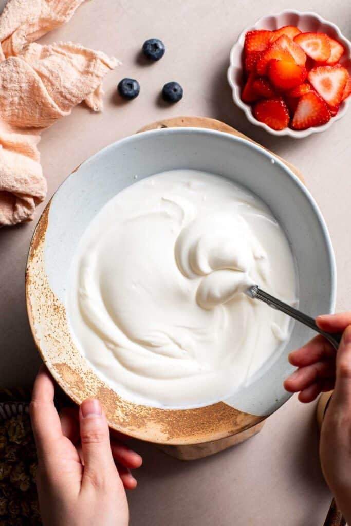 Greek yogurt being stirred in a white bowl to make frozen yogurt bark