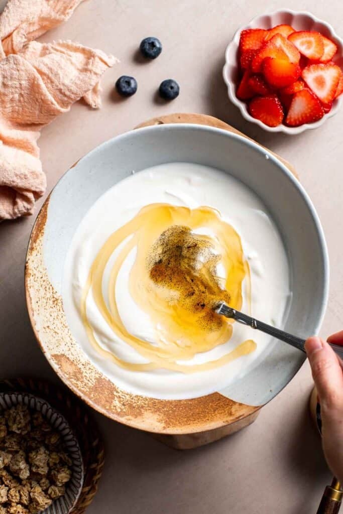 Greek yogurt with honey and vanilla being stirred in a white bowl