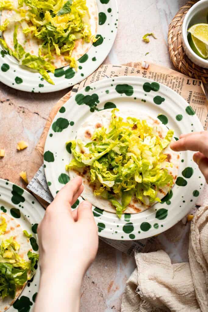 Adding shredded cabbage to a warm tortilla.