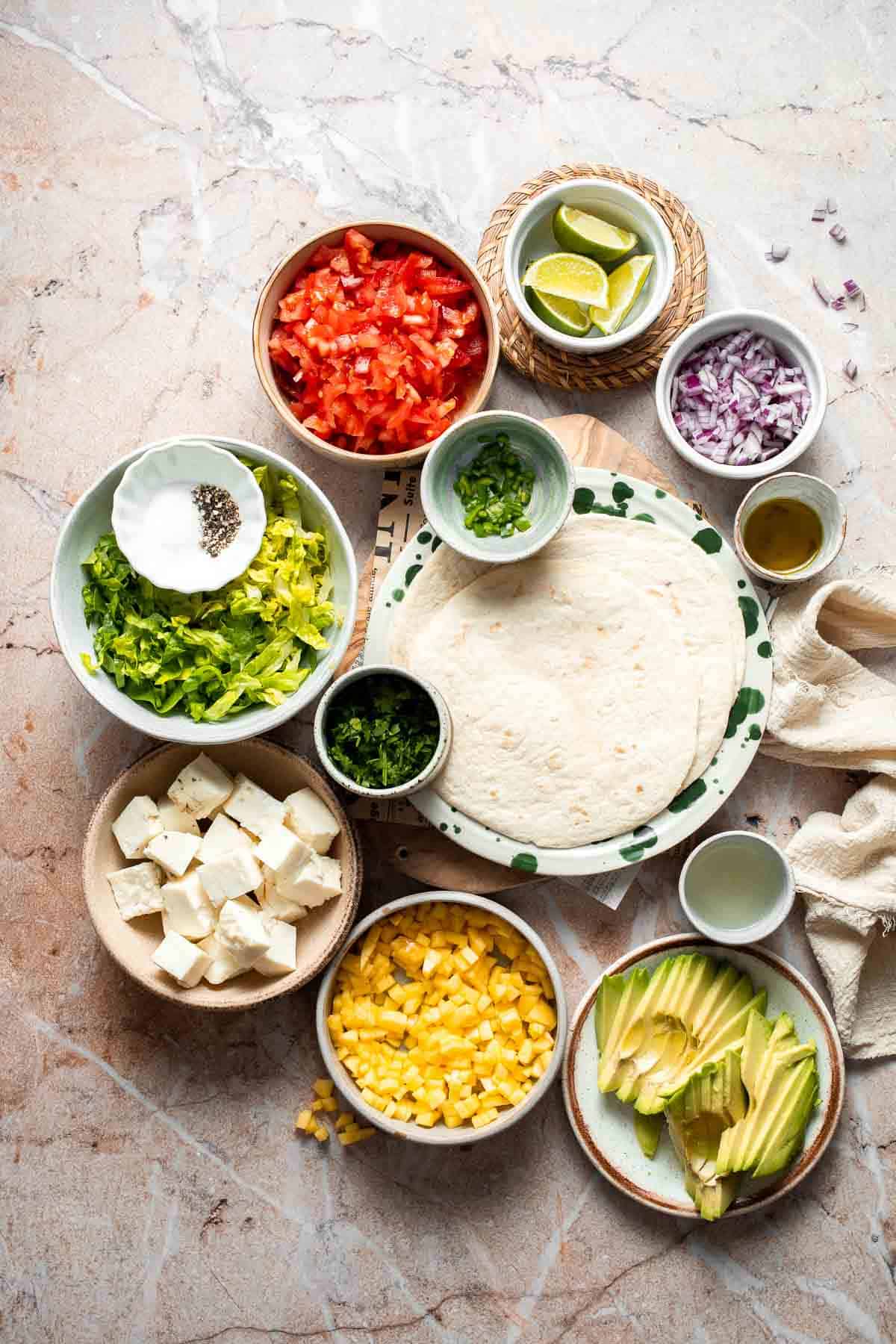 Ingredients for Halloumi Tacos including halloumi, tortillas, avocado, cabbage, tomatoes, mango, red onion, cilantro, and lime.
