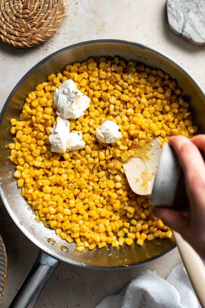 Honey being added to cooked corn in a skillet