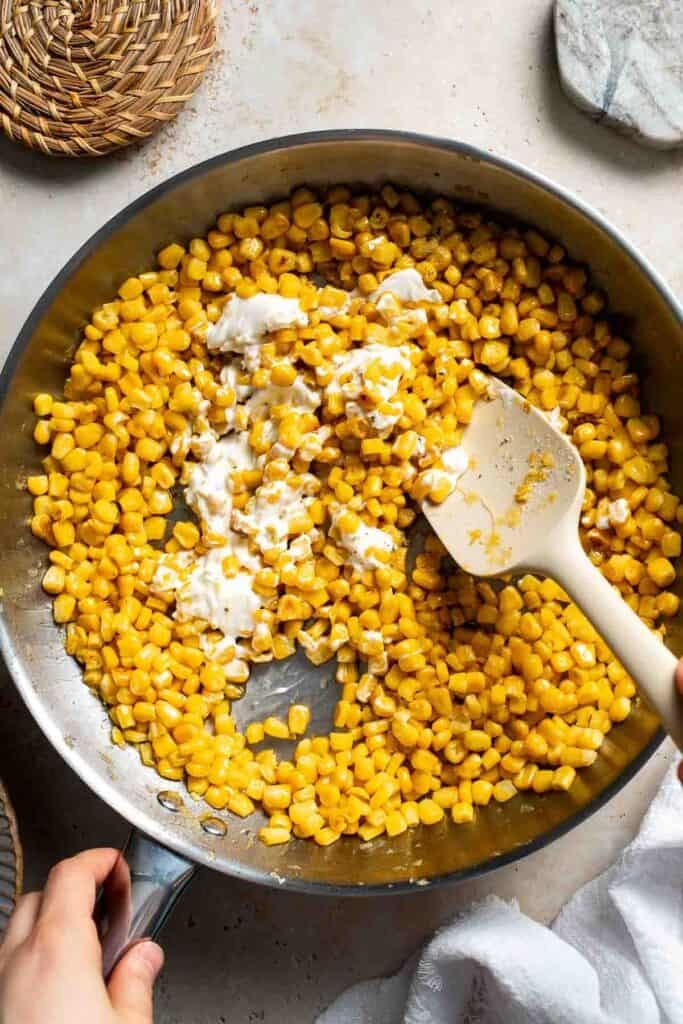 Cream cheese and honey being stirred into corn in a skillet