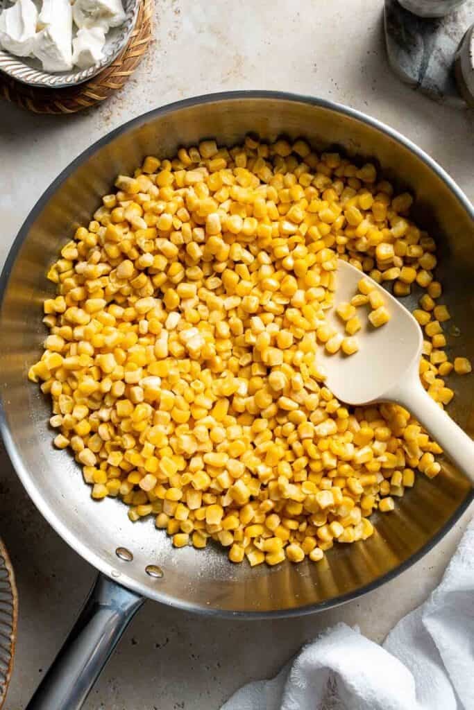 Corn being stirred in melted butter in a skillet with a spatula