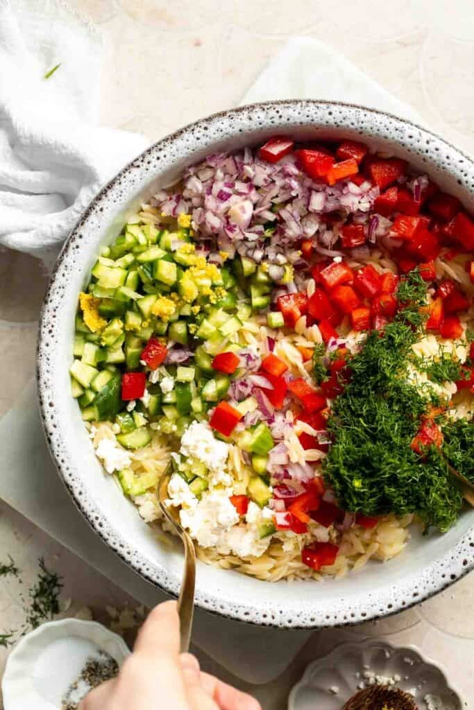 Tossing orzo with cucumber, red pepper, red onion, feta, dill, and lemon dressing.