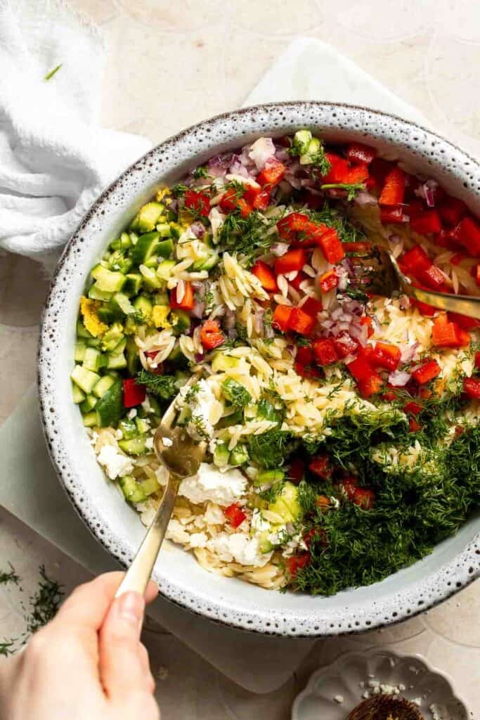 Tossing orzo with cucumber, red pepper, red onion, feta, dill, and lemon dressing.