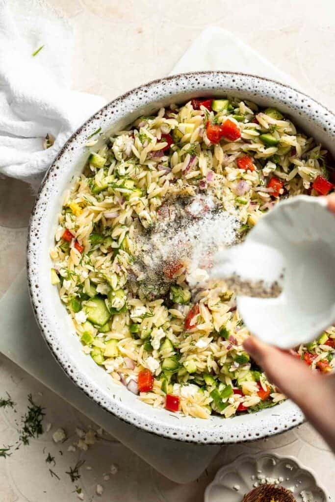 Adding salt and pepper to Lemon Orzo Salad.