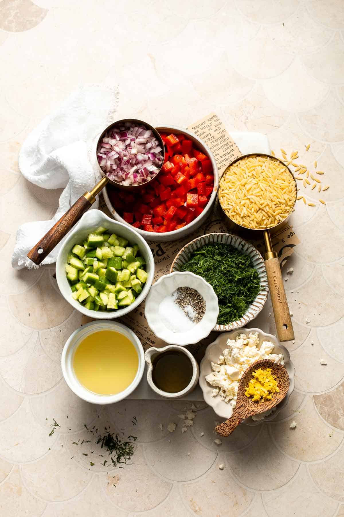 Ingredients for Lemon Orzo Salad including orzo, cucumber, red bell pepper, red onion, feta, dill, lemon, and olive oil.