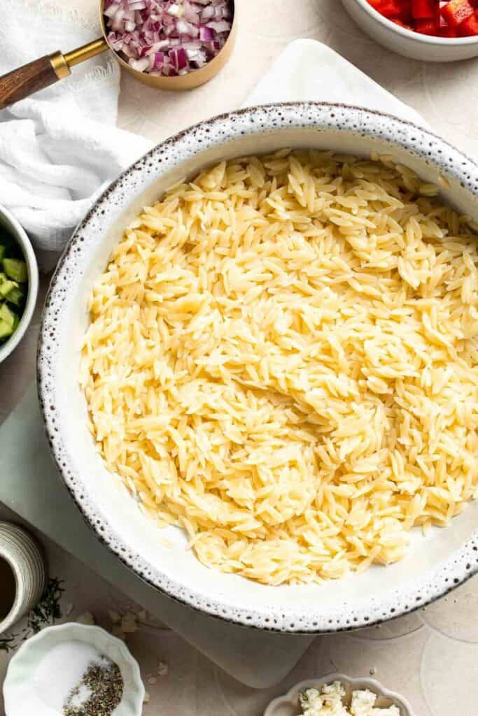 Cooled orzo pasta in a large mixing bowl.