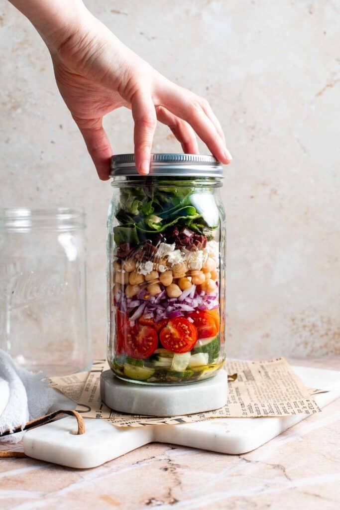 Closing the lid of the assembled Mediterranean mason jar salad