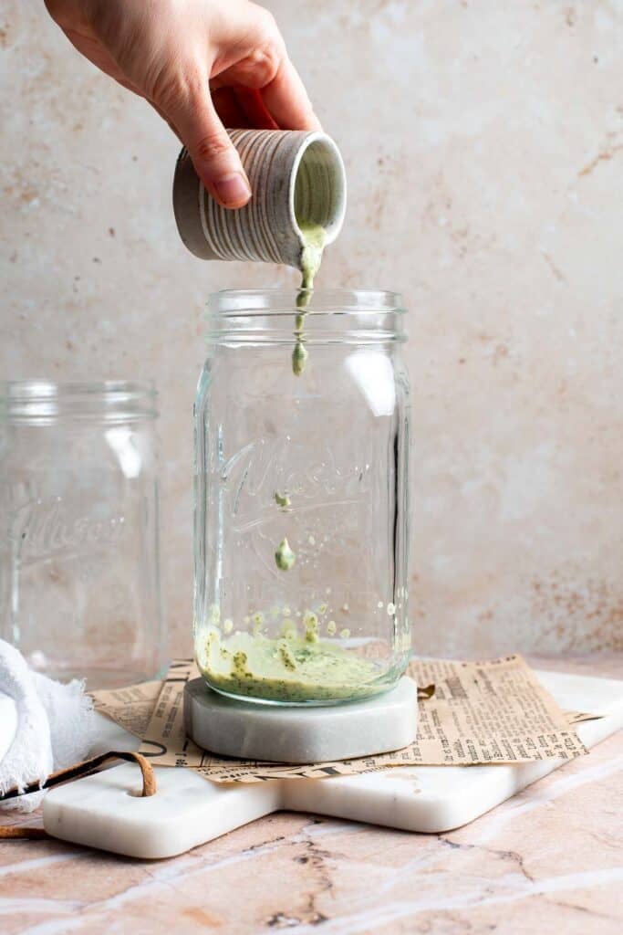 Cilantro lime dressing being poured into the bottom of a mason jar