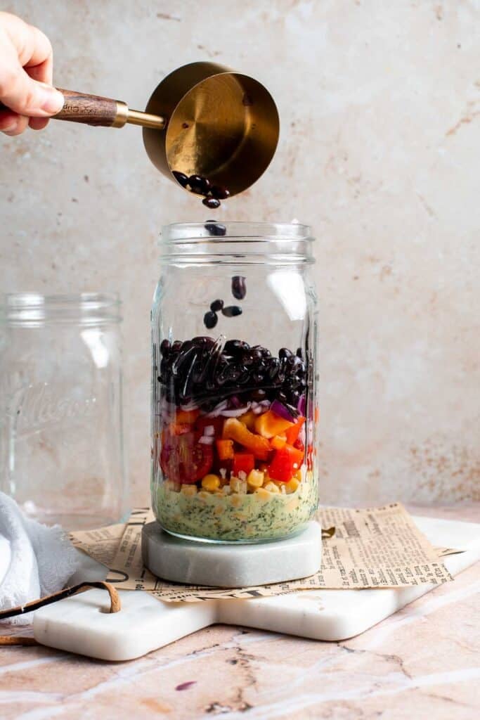 Black beans being spooned into a mason jar salad with a small scoop