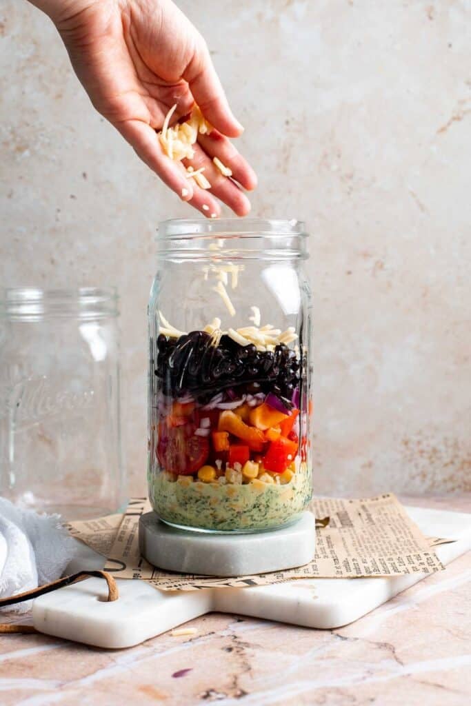 Corn being sprinkled into a layered Southwest mason jar salad