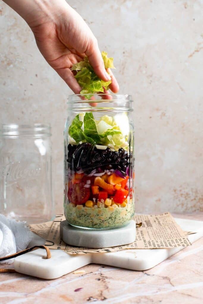 Chopped romaine lettuce being added to a mason jar salad