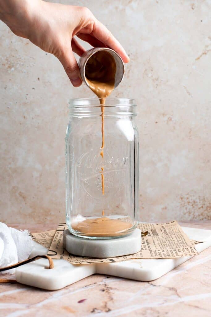 Thai peanut dressing being poured into the bottom of a mason jar