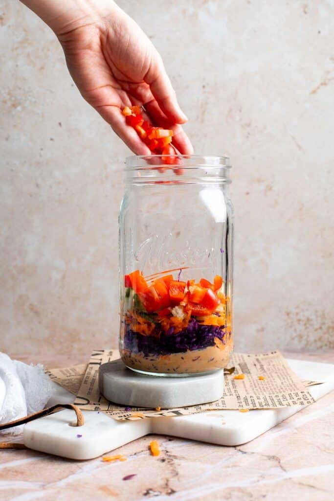Diced red bell pepper being added to an Asian peanut mason jar salad