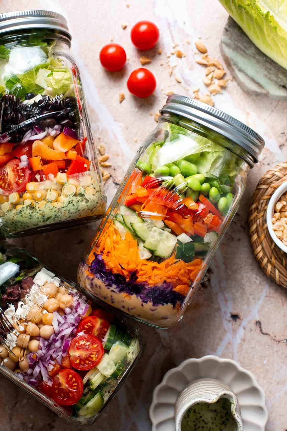 Overhead view of three mason jar salads next to bowls of ingredients