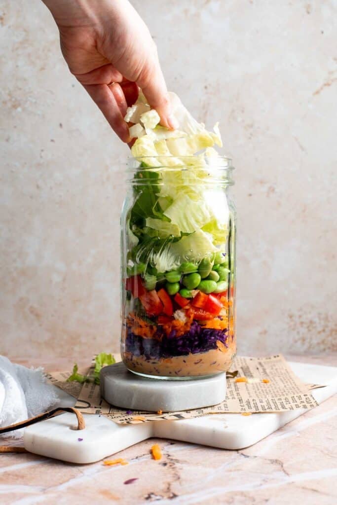 Chopped romaine lettuce being added to an Asian peanut mason jar salad
