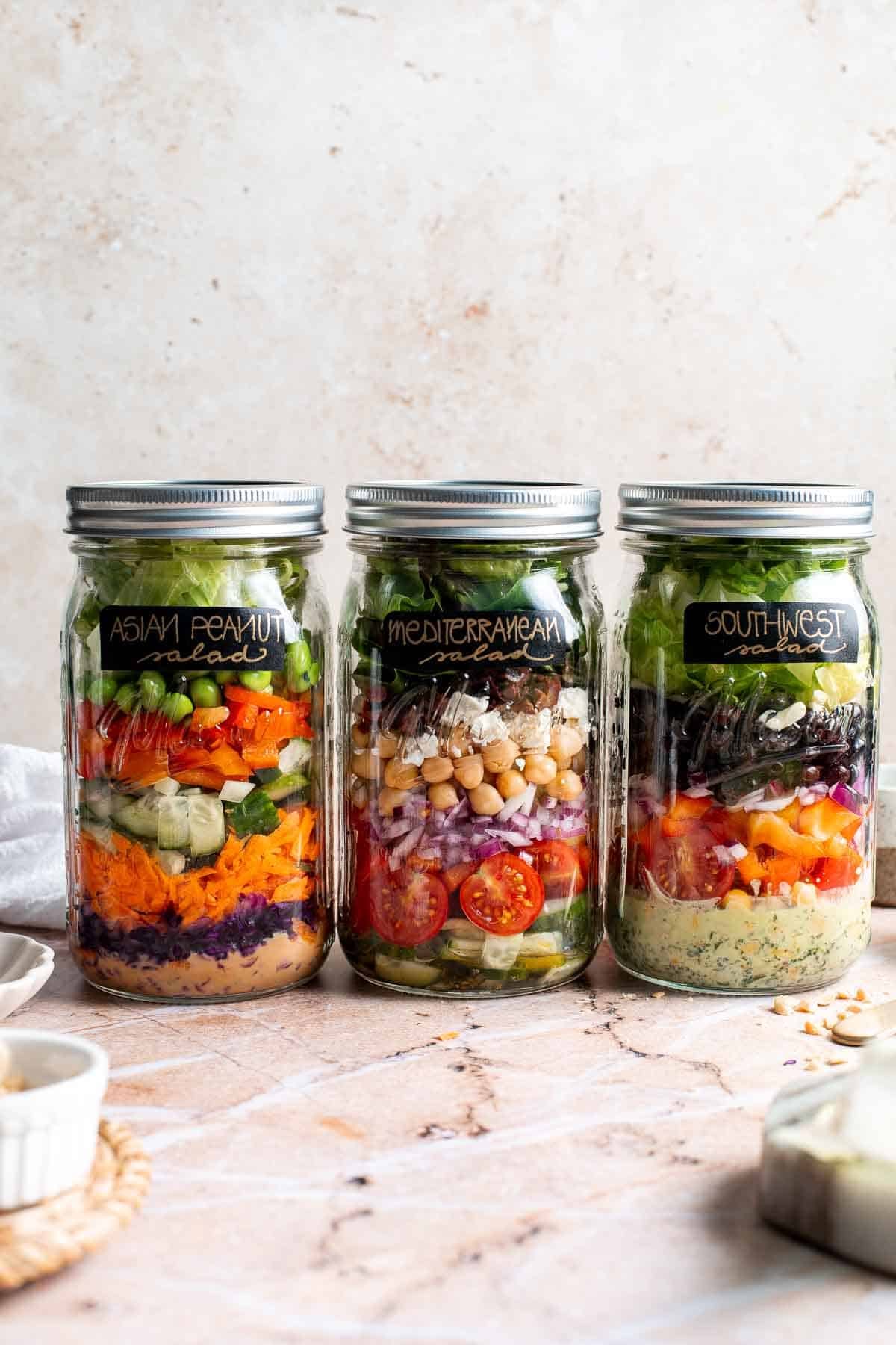 Three layered mason jar salads lined up on a marble countertop