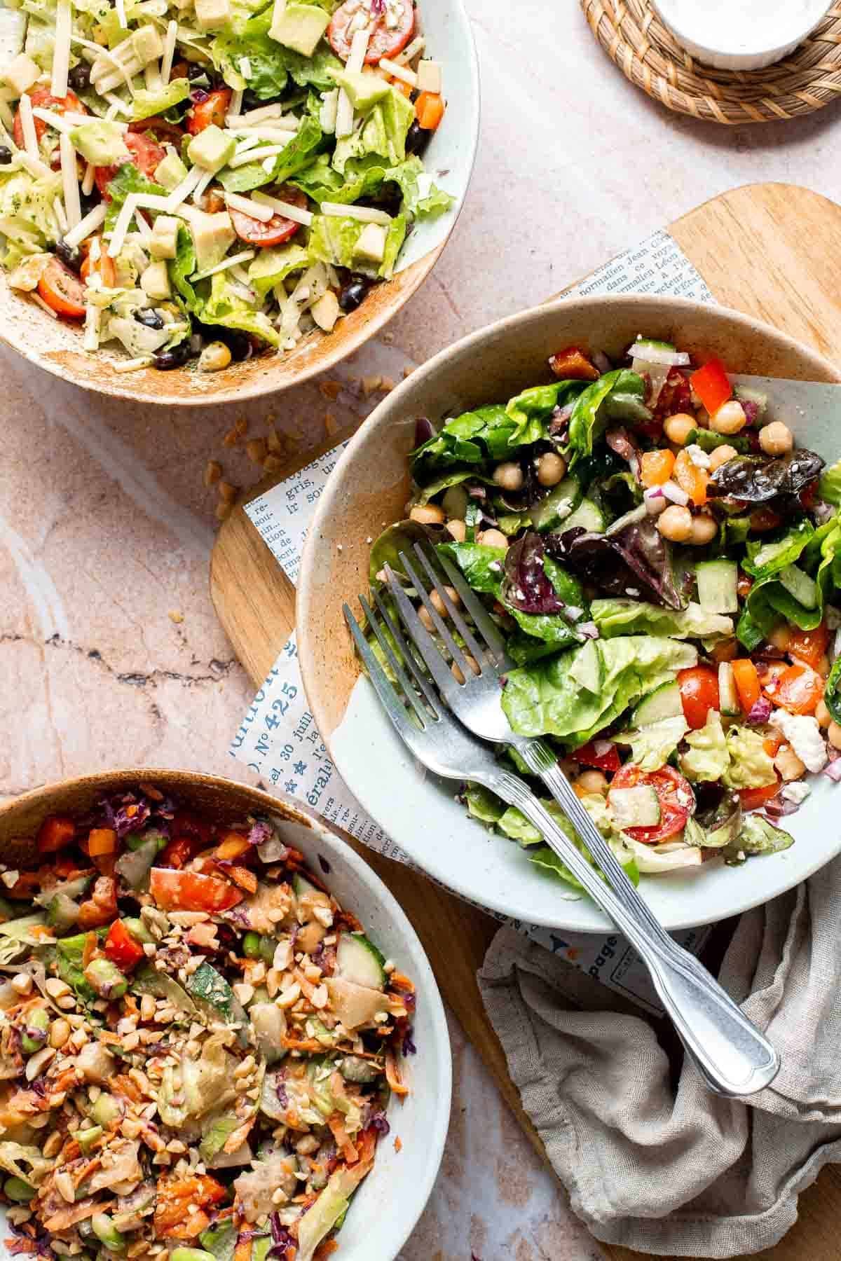 Mason jar salad poured into a bowl, served alongside bowls of the other variations