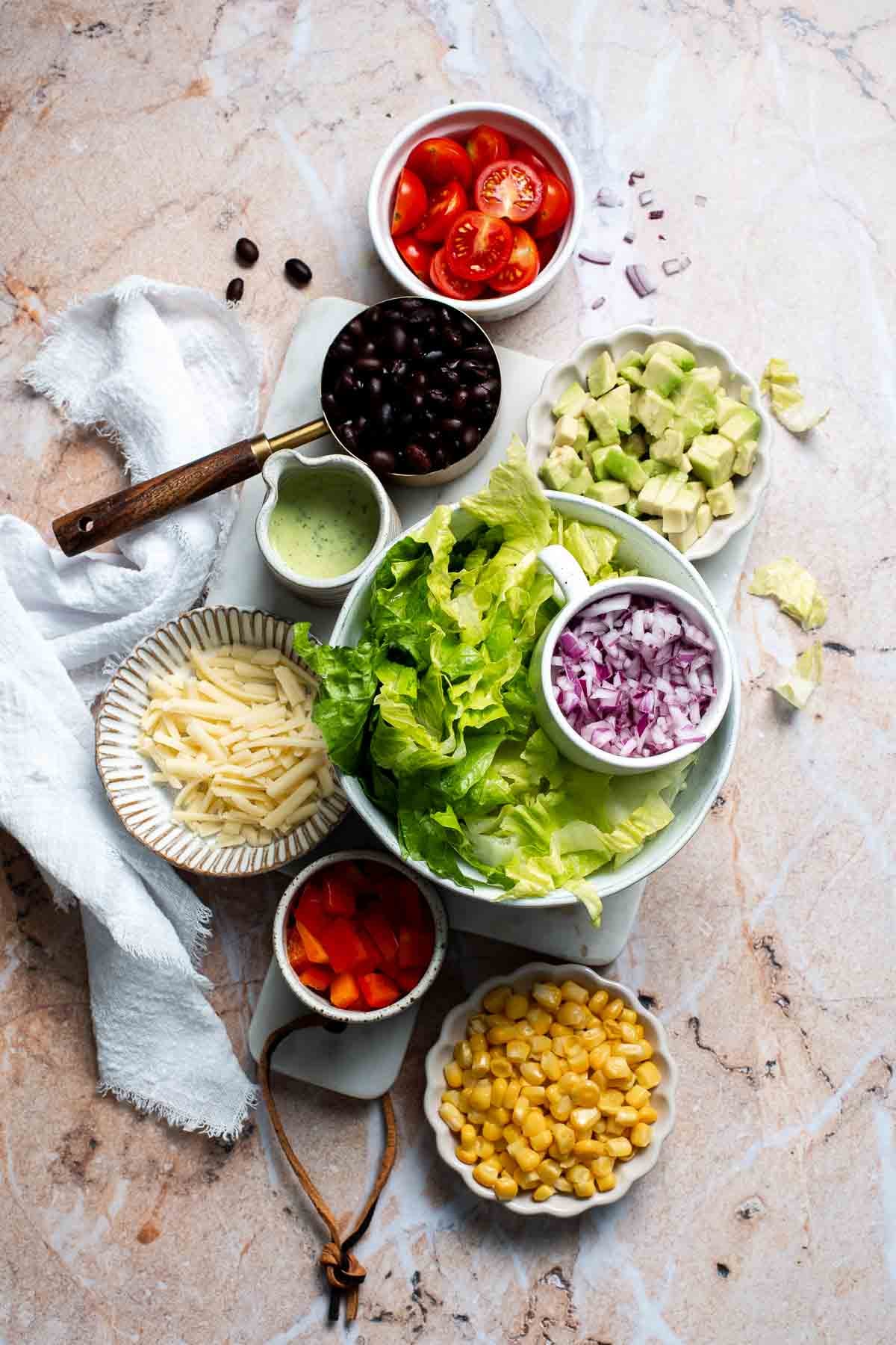 Overhead view of Southwest mason jar salad ingredients including corn, black beans, and cheddar cheese in bowls