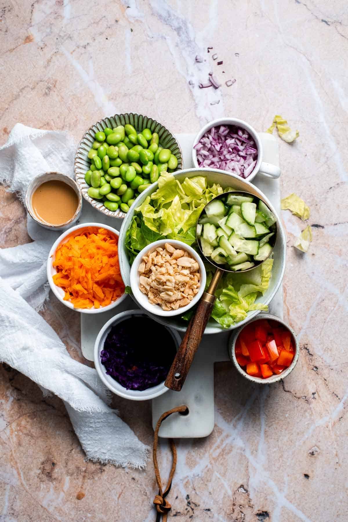 Overhead view of Asian peanut mason jar salad ingredients including cabbage, carrots, and edamame in bowls
