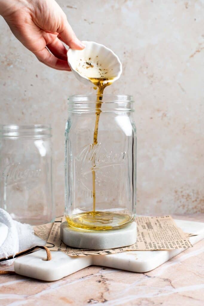 Greek salad dressing being poured into a mason jar to start layering a salad