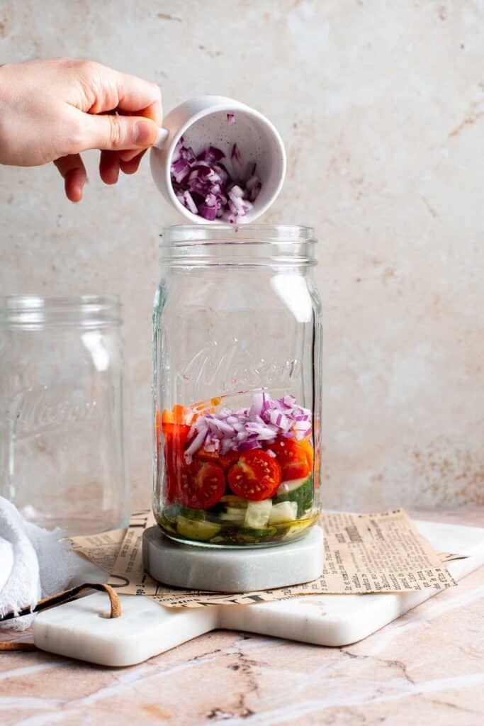 Red onion being poured into a mason jar on top of the salad dressing