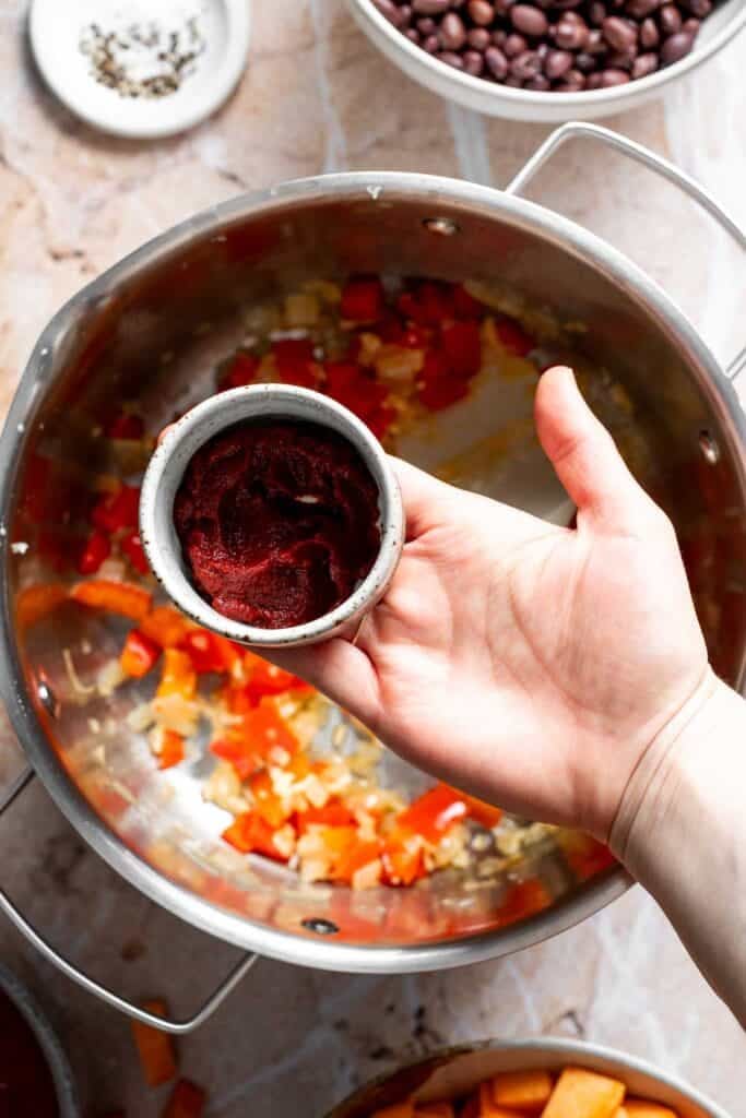 Adding tomato paste to sautéed vegetables in a pot