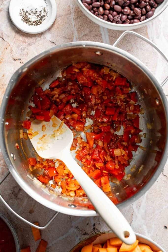 Tomato paste being stirred into sautéed vegetables in a pot
