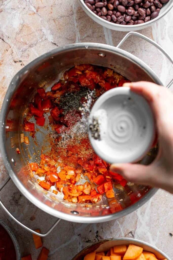 Adding salt and pepper to the pot of veggies.