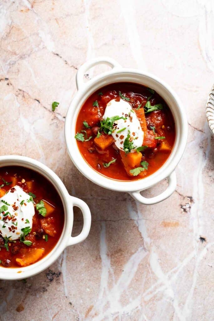 Two bowls of sweet potato black bean chili topped with sour cream and fresh herbs