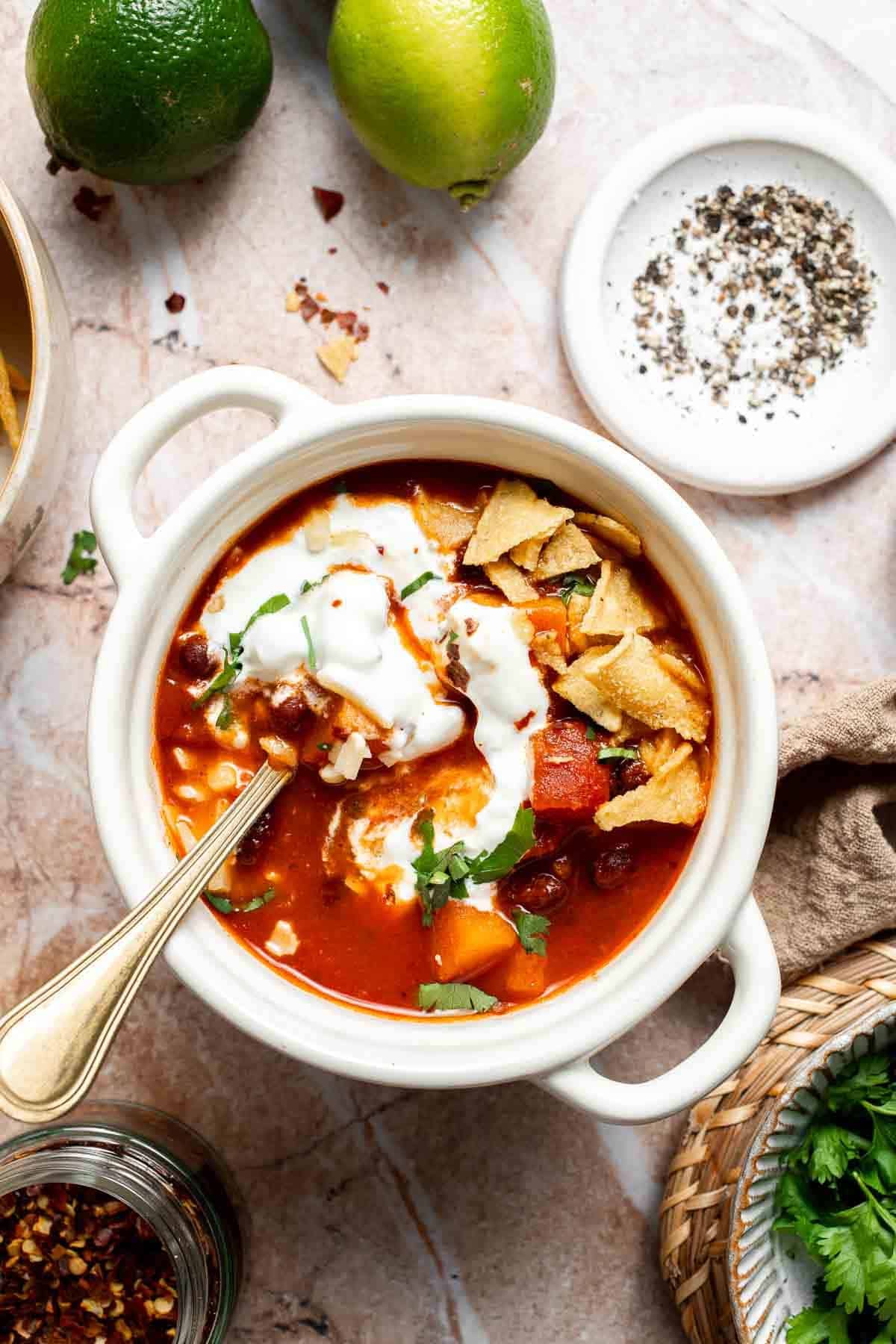 Bowl of sweet potato black bean chili garnished with sour cream, cilantro, tortilla chips, and lime wedges