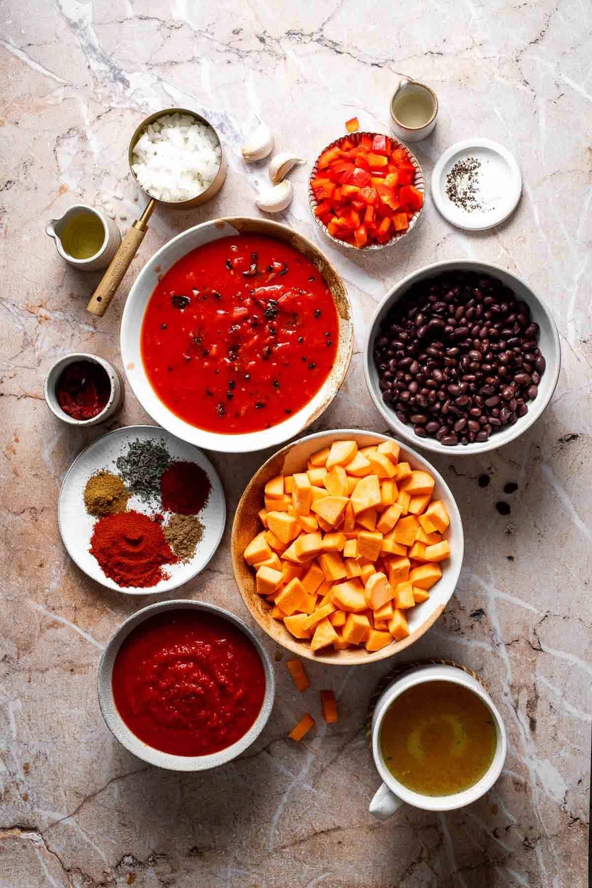Ingredients for sweet potato black bean chili including spices, tomatoes, black beans, and tortilla chips arranged on a marble surface