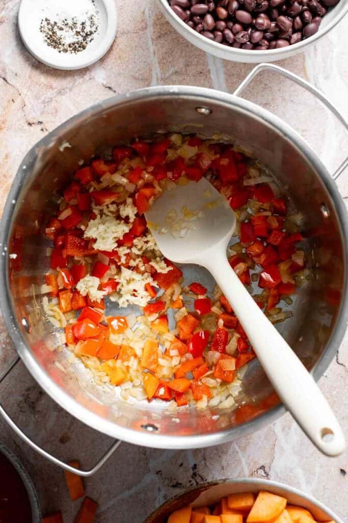 Adding garlic to sautéed diced onion and bell pepper in a pot
