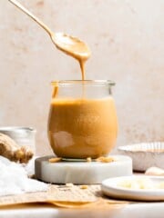 Thai peanut dressing being drizzled from a spoon into a glass jar, showing its smooth, pourable consistency
