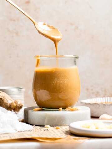 Thai peanut dressing being drizzled from a spoon into a glass jar, showing its smooth, pourable consistency