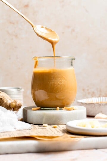 Thai peanut dressing being drizzled from a spoon into a glass jar, showing its smooth, pourable consistency
