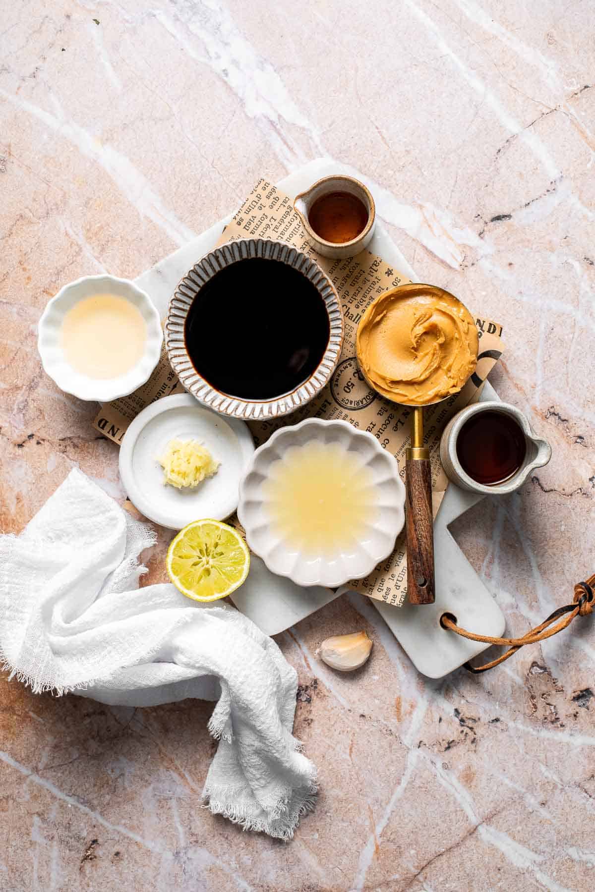 Ingredients for Thai peanut dressing including peanut butter, soy sauce, lime, ginger, and garlic arranged on a marble surface