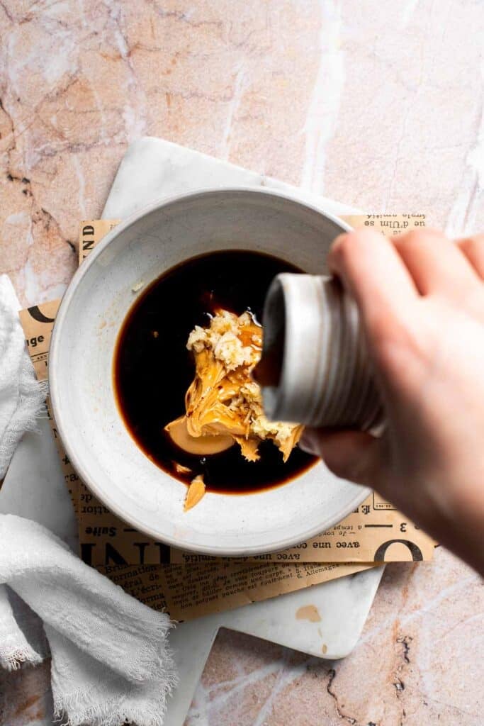 Soy sauce being poured into a bowl with peanut butter to make Thai peanut dressing