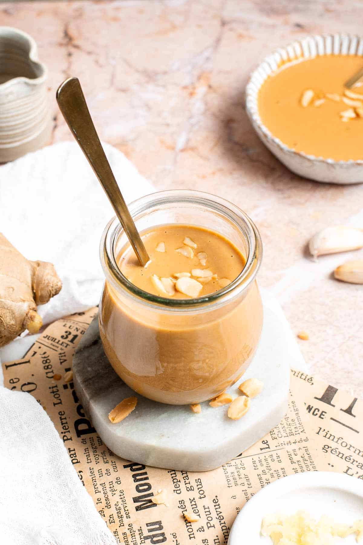 Thai peanut dressing in a glass jar with a spoon, garnished with crushed peanuts