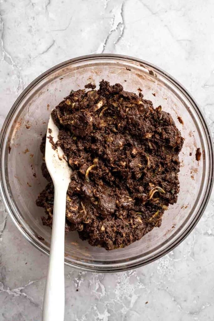 Shredded zucchini being folded into thick chocolate brownie batter