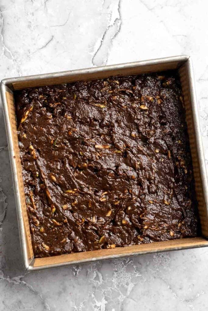 Unbaked zucchini brownie batter spread evenly into a parchment-lined square baking pan