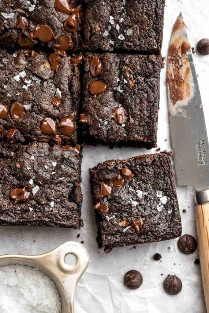 Fudgy zucchini brownie squares on parchment paper next to a knife