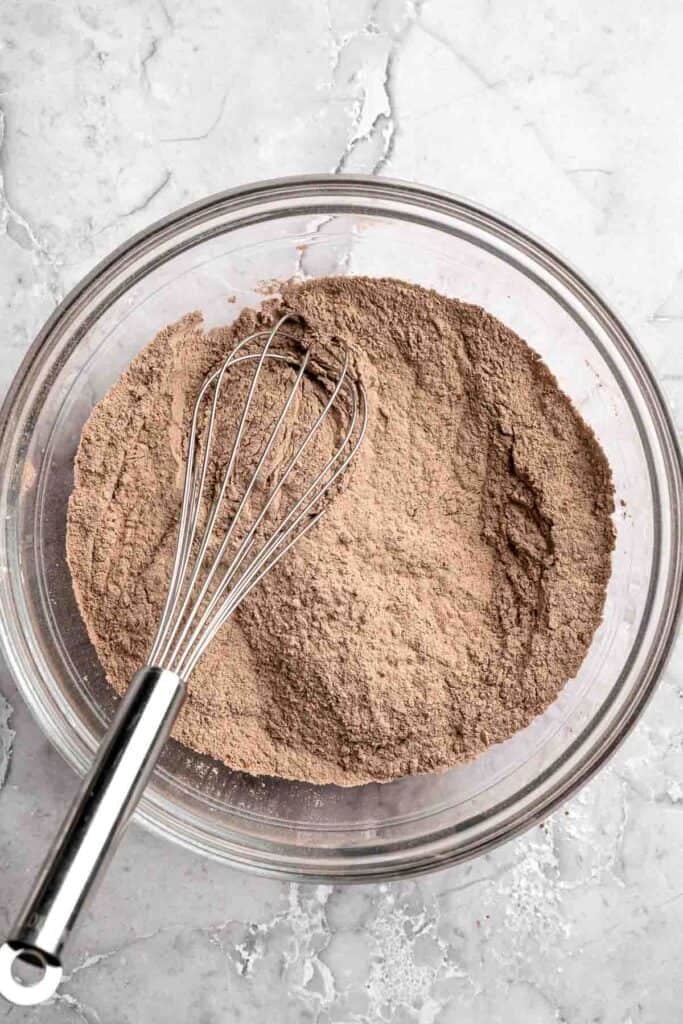 Dry ingredients including flour and cocoa powder whisked together in a glass bowl