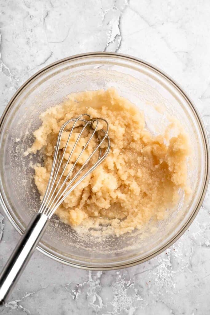 Wet ingredients including oil, sugar, and vanilla extract whisked together in a glass bowl