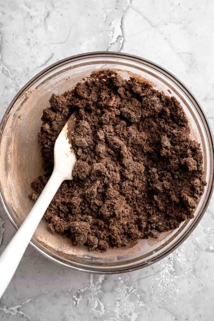 Thick, crumbly zucchini brownie batter being stirred with a spoon in a glass bowl